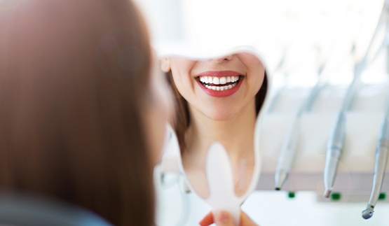 Woman looking at her smile in a mirror in dental office
