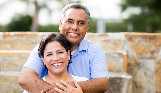 Smiling older man and woman holding each other in front of brick staircase