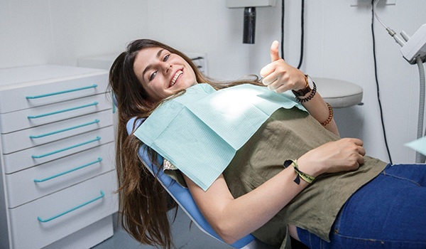Woman smiling in dental chair while giving a thumbs up
