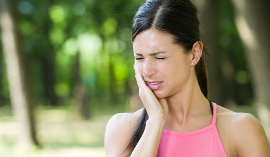 Woman holding her jaw in pain while outdoors