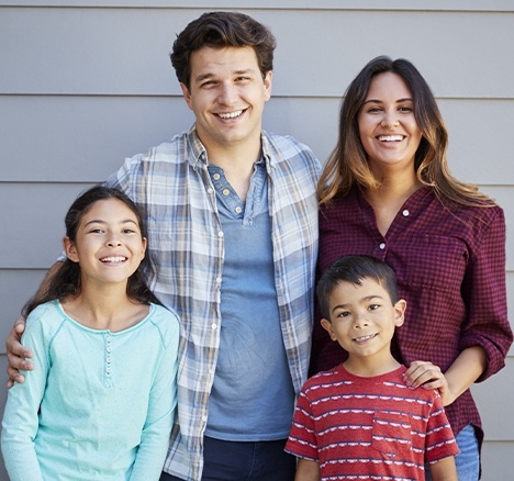 Family of four smiling and standing in front of garage door