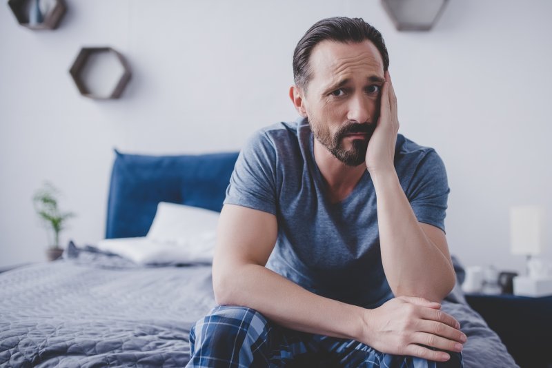 A man with a nighttime toothache sitting on a bed